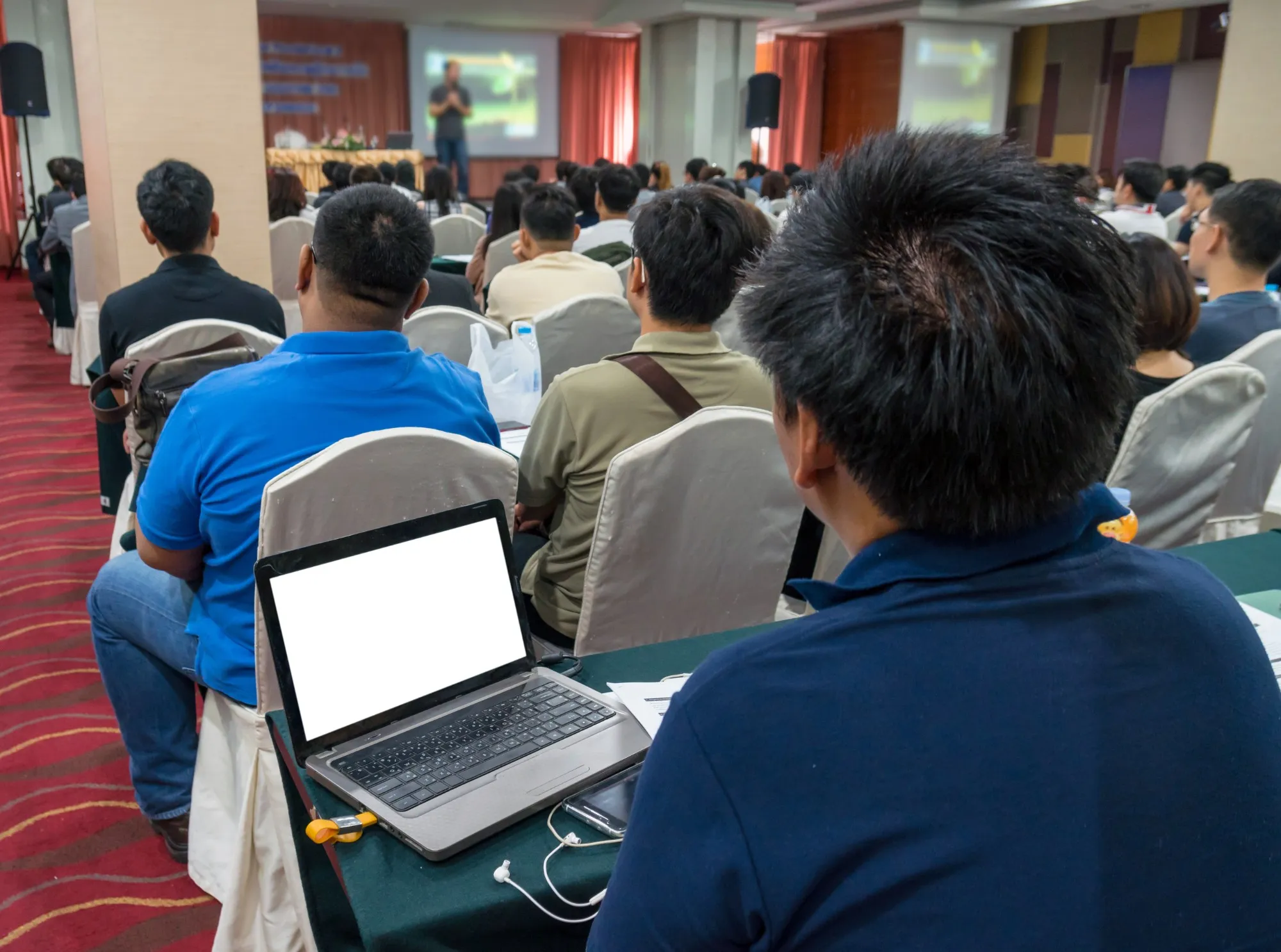 Attendees at an on-site AI workshop, seated in rows with laptops open, watching a presentation